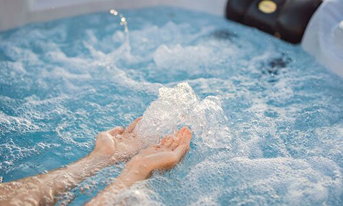 Hands feel the bubbles of a hot tub.