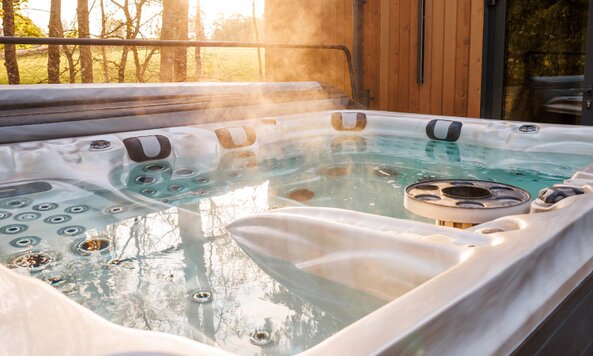 A steaming hot tub with the lid open on an outside wood patio.
