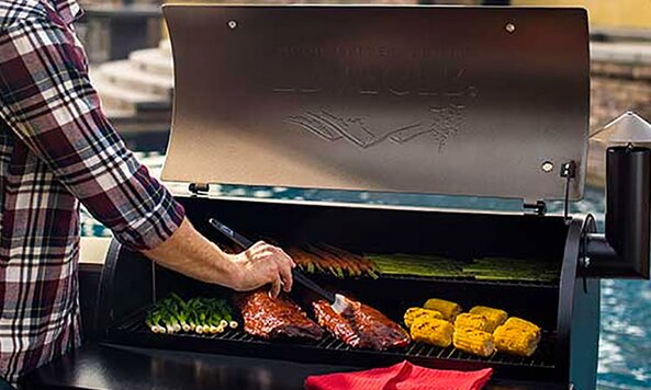 A person wearing a plaid shirt basted a piece of meat on the grill.