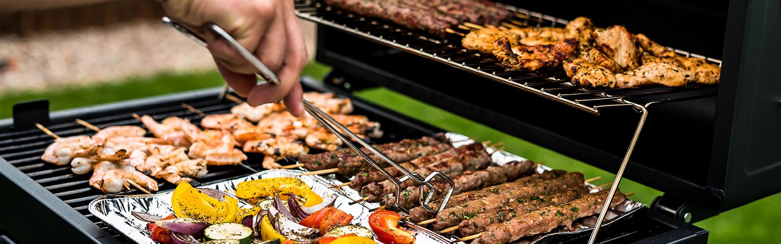 A grill cooking a variety of food, including veggies, skewers, chicken, and shrimp. 
