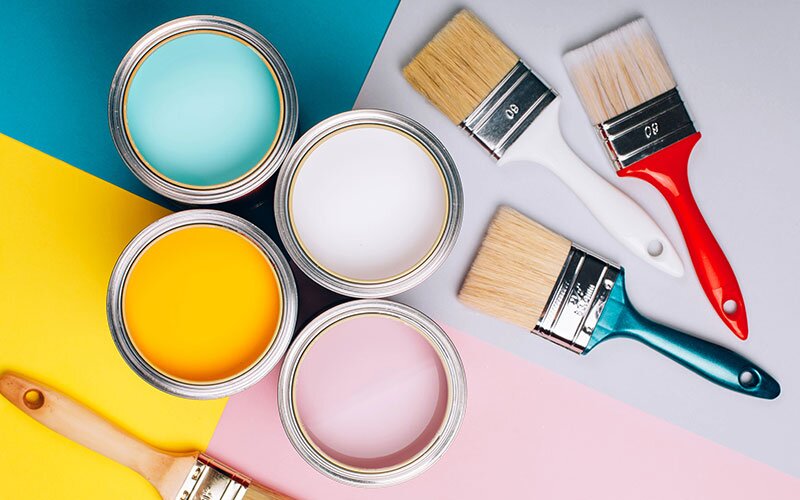Paint cans match their background. Brushes lay beside. 