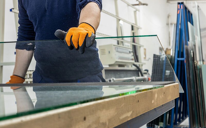 A worker wearing protective gloves holds a freshly cut piece of glass. 