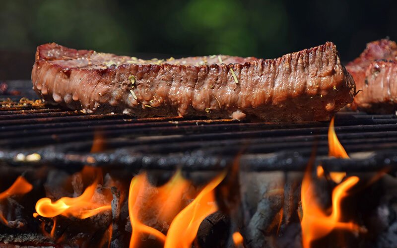 A perfect steak grilling on an open flame on an outdoor grill.