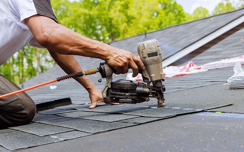 A roofer uses a roofing gun to attach shingles to a roof.