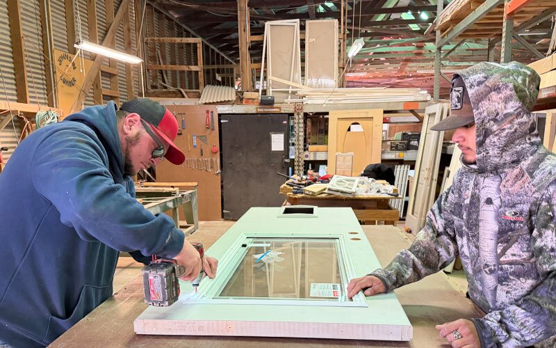 Workers installing hardware on an exterior door available at Johnston Wholesale Lumber.