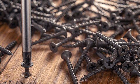A pile of nails on a wooden surface, a screwdriver screws in one of the nails.
