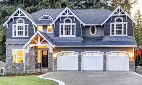 A home exterior with wood siding, stone faux stone veneer, beautiful windows, and a three-car garage.