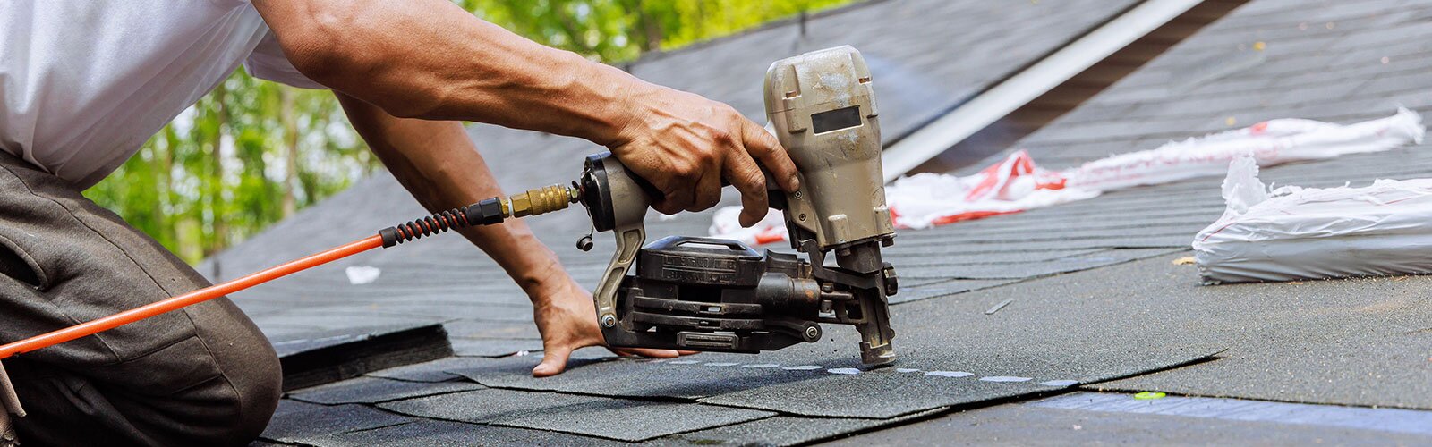 A roofer uses a roofing gun to attach shingles to a roof.
