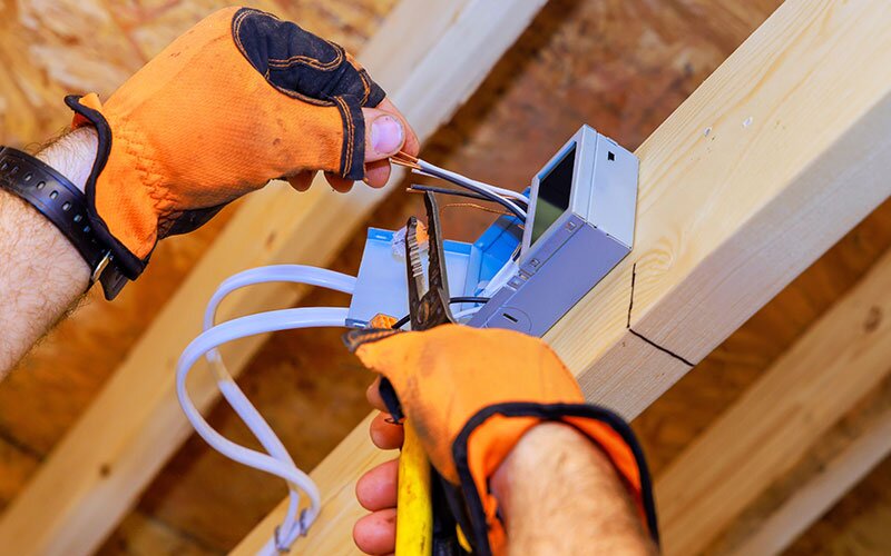 Hands of electrican wearing orange gloves cut wires in preparation for the receptacle.