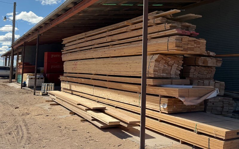 A large amount of lumber is stacked under a covered exterior storage area at Johnson Wholesale Lumber.