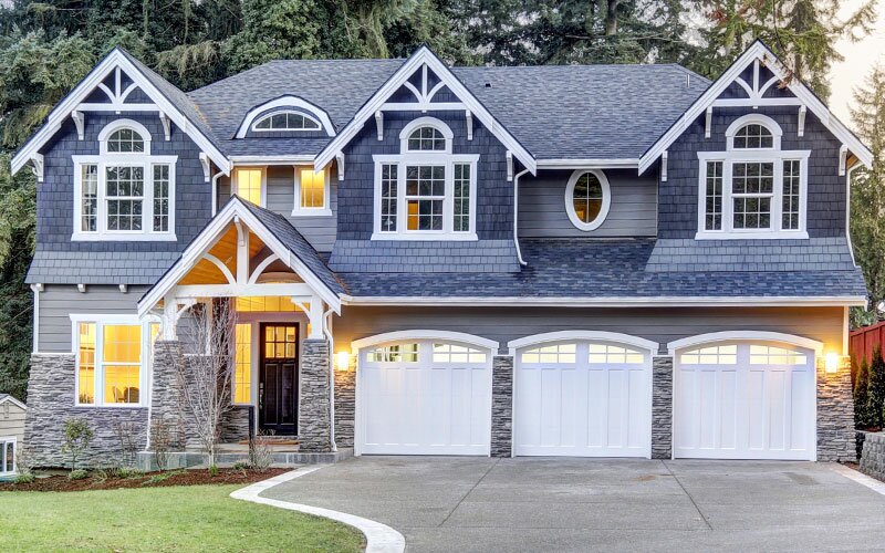 A home exterior with wood siding, stone faux stone veneer, beautiful windows, and a three-car garage.