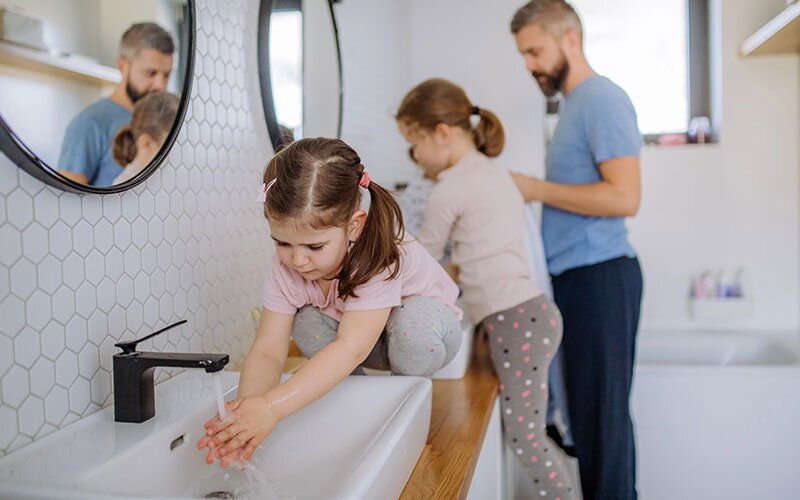 A little girl washes her hands in the bathroom during the morning routine in her home.