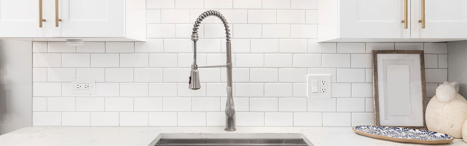 A white kitchen counter and cabinets with an undermount sink, faucet, and lighting.