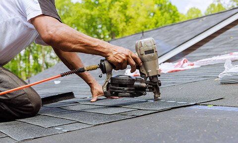 A roofer uses a roofing gun to attach shingles to a roof.