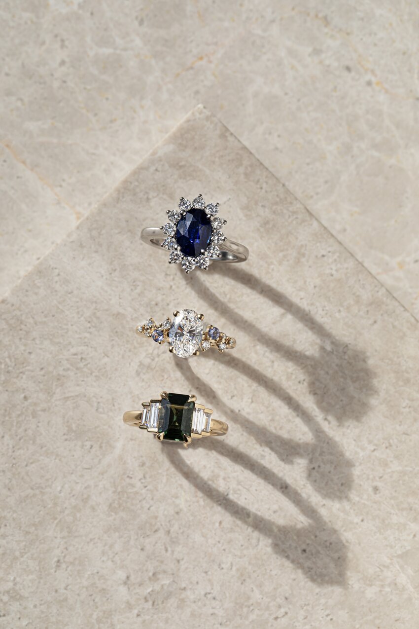 Luxury gemstone rings with sapphire, diamond, and green centre stones on stone.