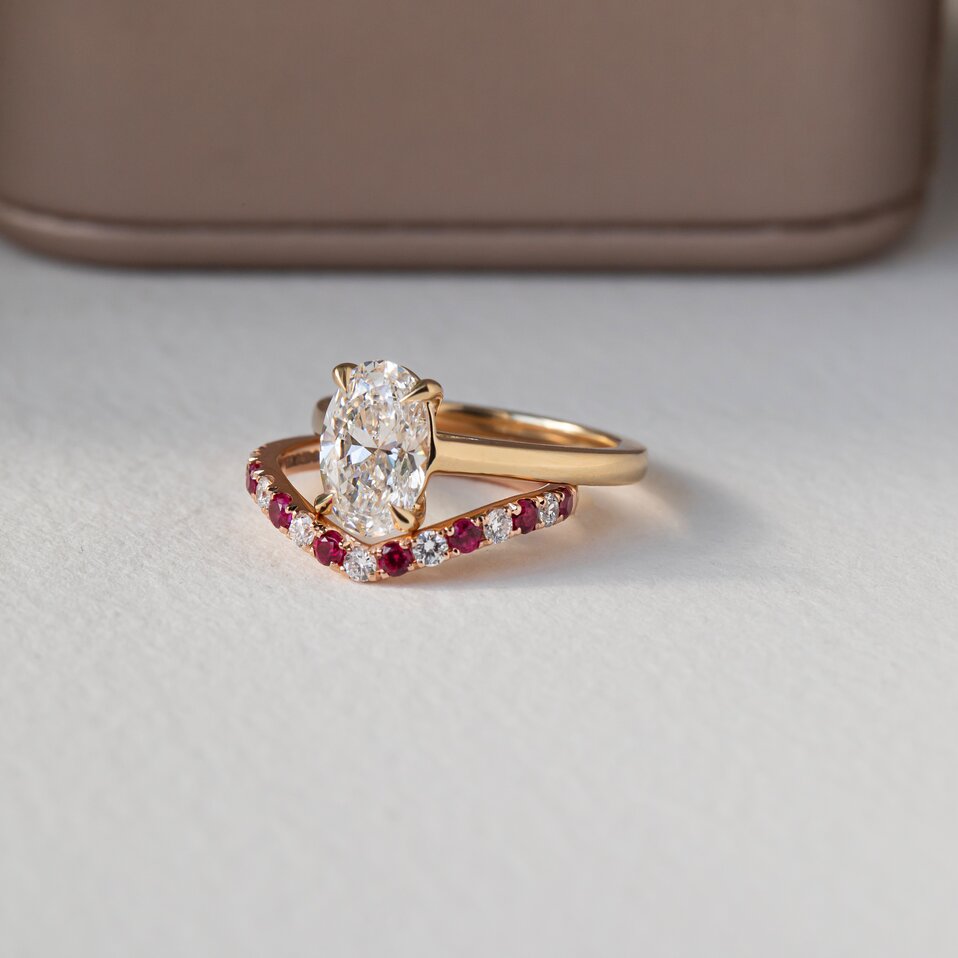 An oval cut diamond ring paired with a V shaped ruby and diamond band.