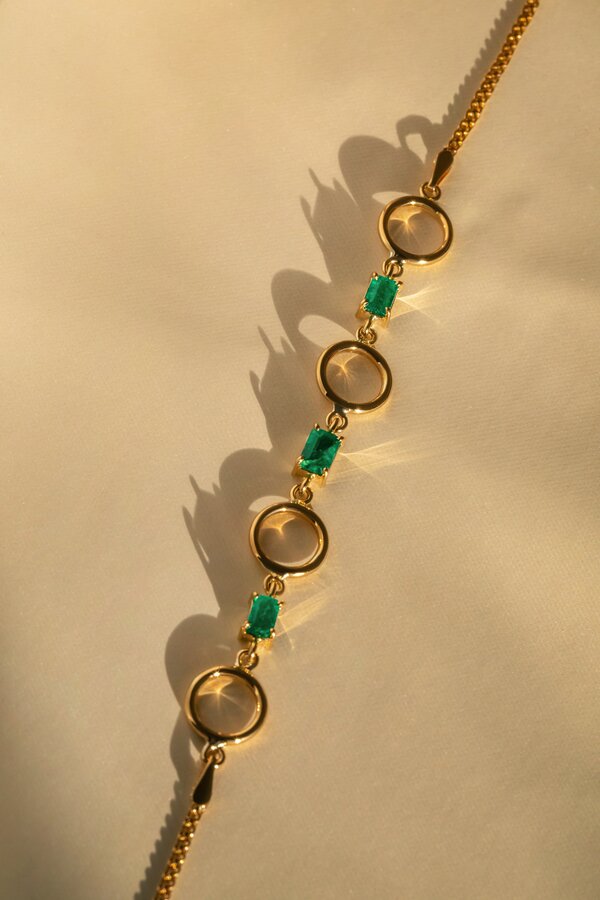 Bespoke yellow gold bracelet with emerald-cut green gemstones and circular link design