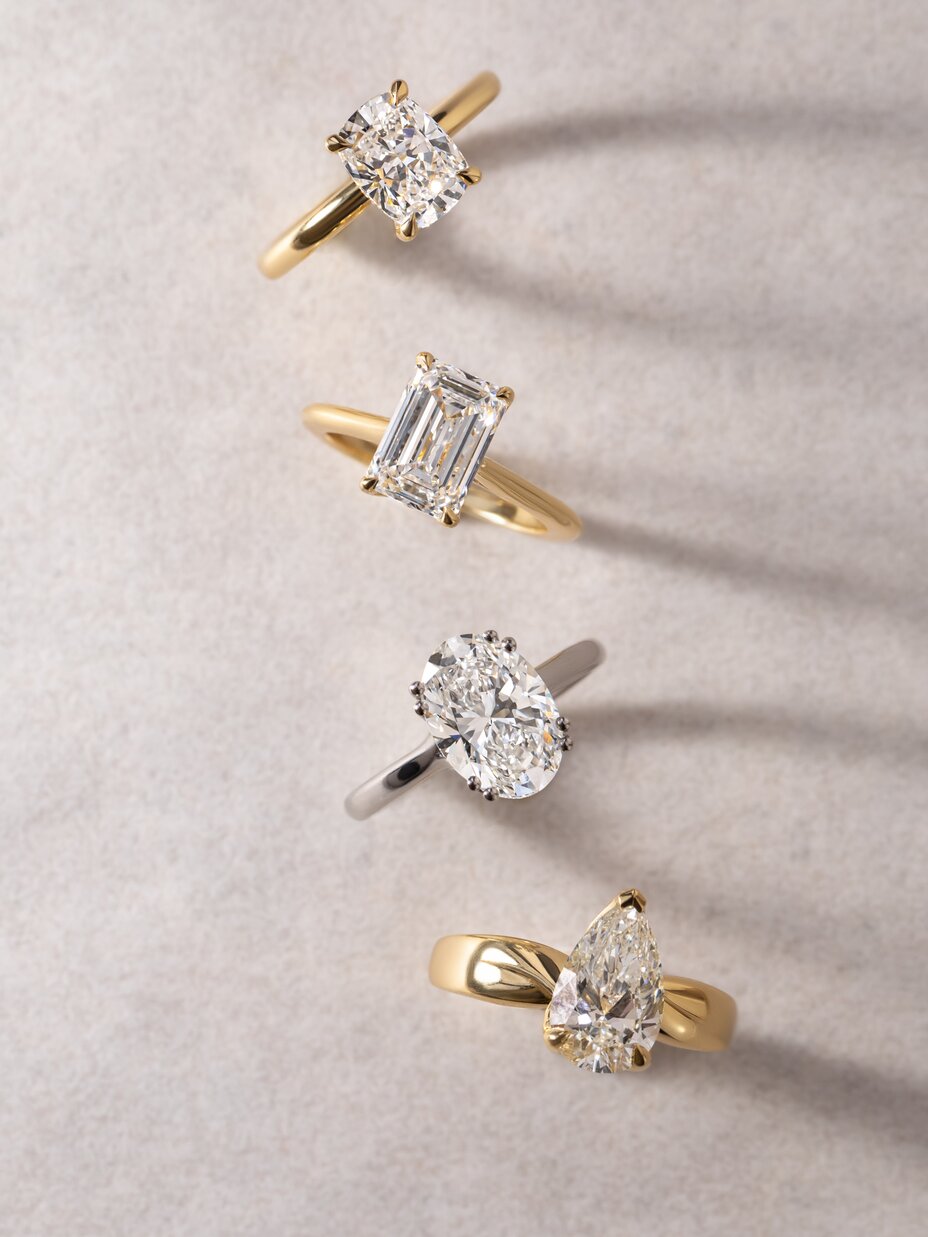 Diamond rings showcasing an elongated cushion cut, an emerald cut, and a pear-cut diamond in yellow gold, along with an oval-cut diamond set in white gold