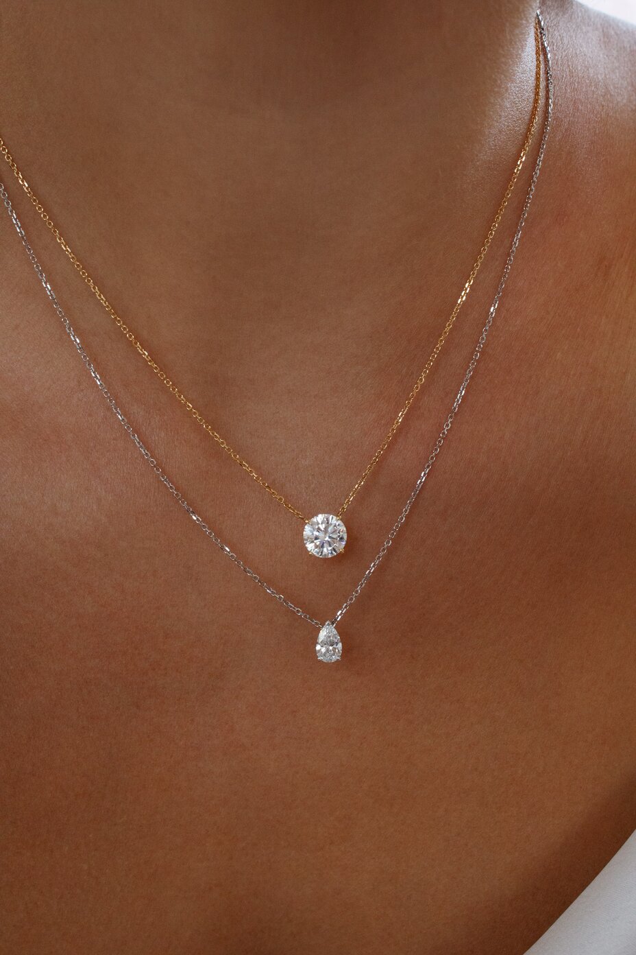 Round and pear shaped diamond solitaire pendant necklaces layered on a model.