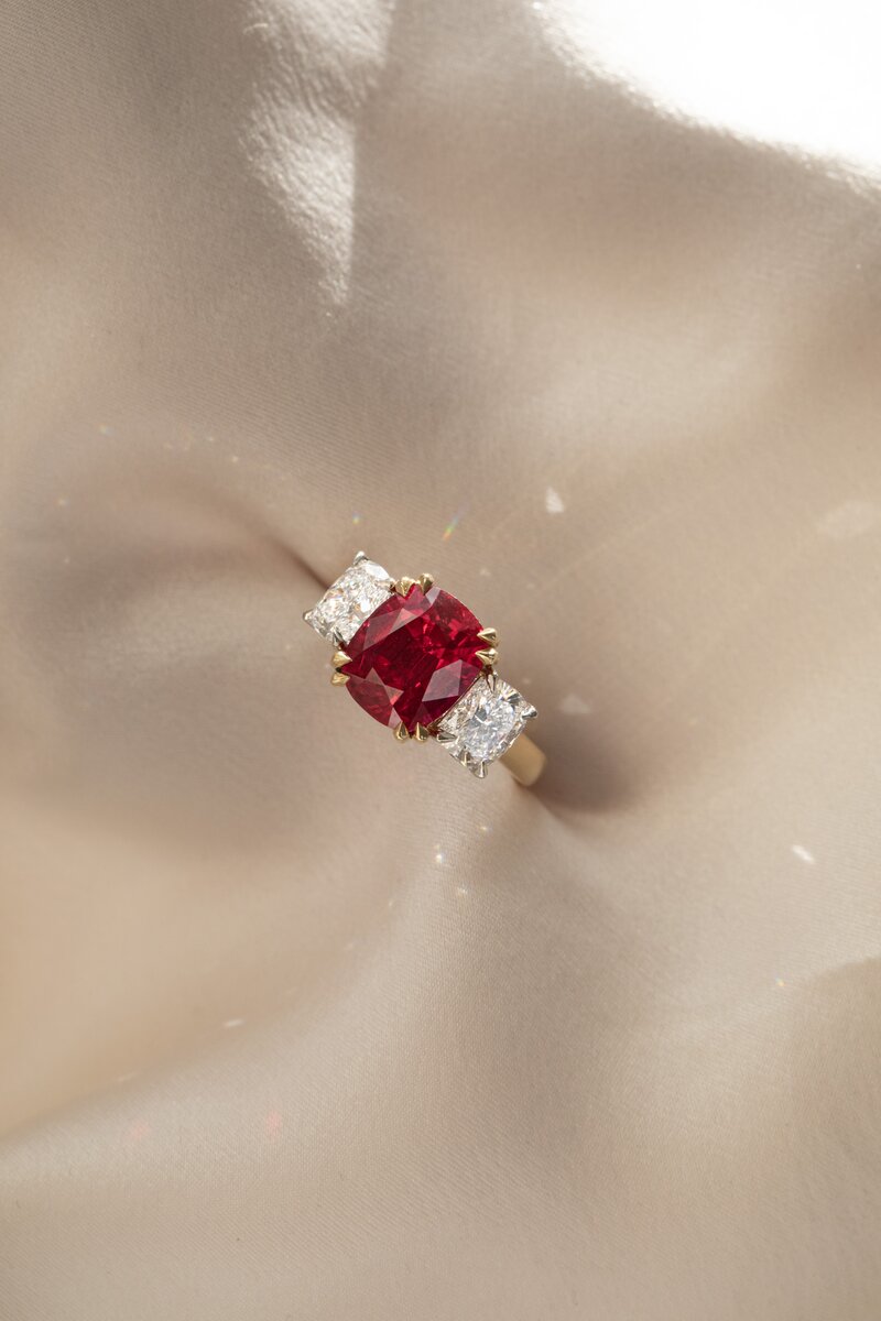 Bespoke three-stone ruby ring with side diamonds on a hand.