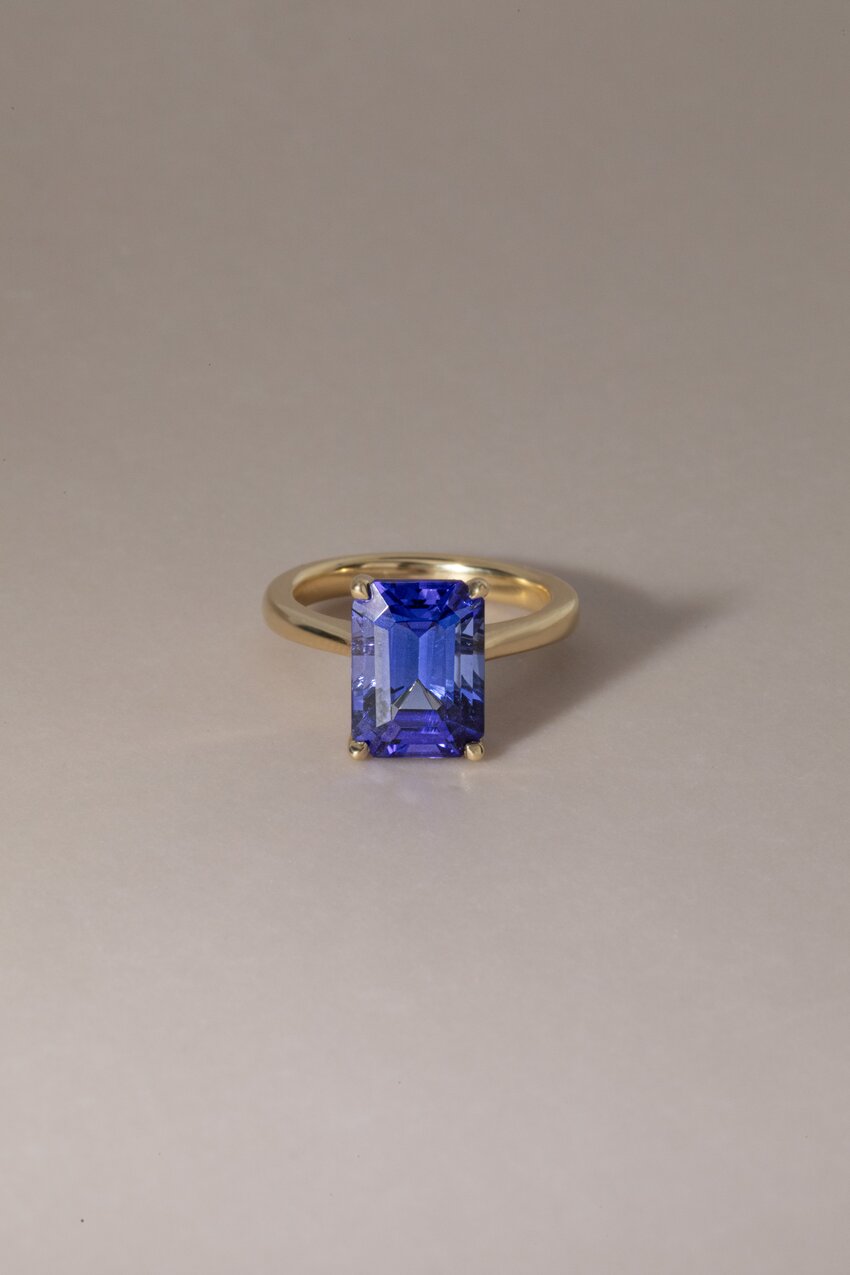 Yellow gold solitaire ring featuring a large, vibrant emerald-cut blue tanzanite gemstone.