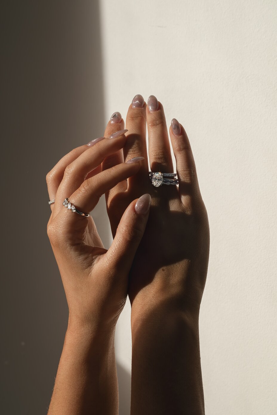 model hands wearing mixed diamond rings and an oval engagement ring