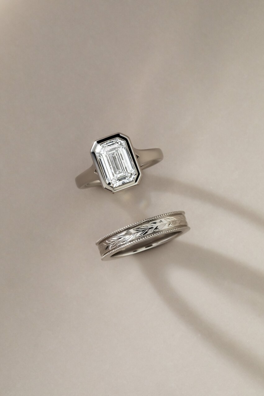 platinum bridal set featuring an engraved floral wedding band and a bezel set emerald diamond ring