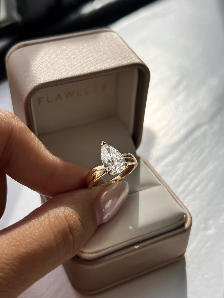 hand holding a pear diamond solitaire engagement ring in yellow gold with a chunky, bow shaped band