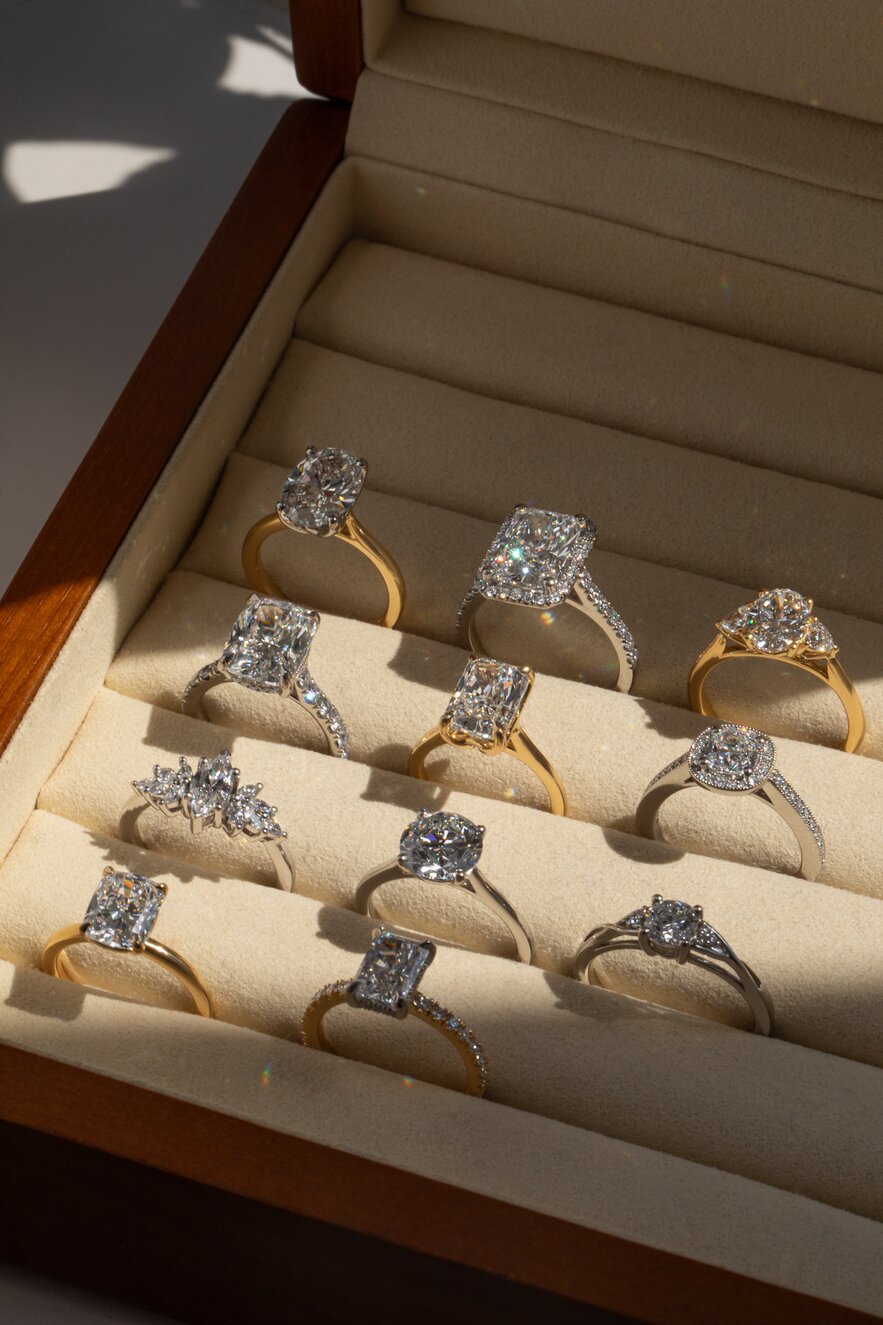 ring display box with engagement rings in multiple styles and mixed metals featuring various diamond shapes.