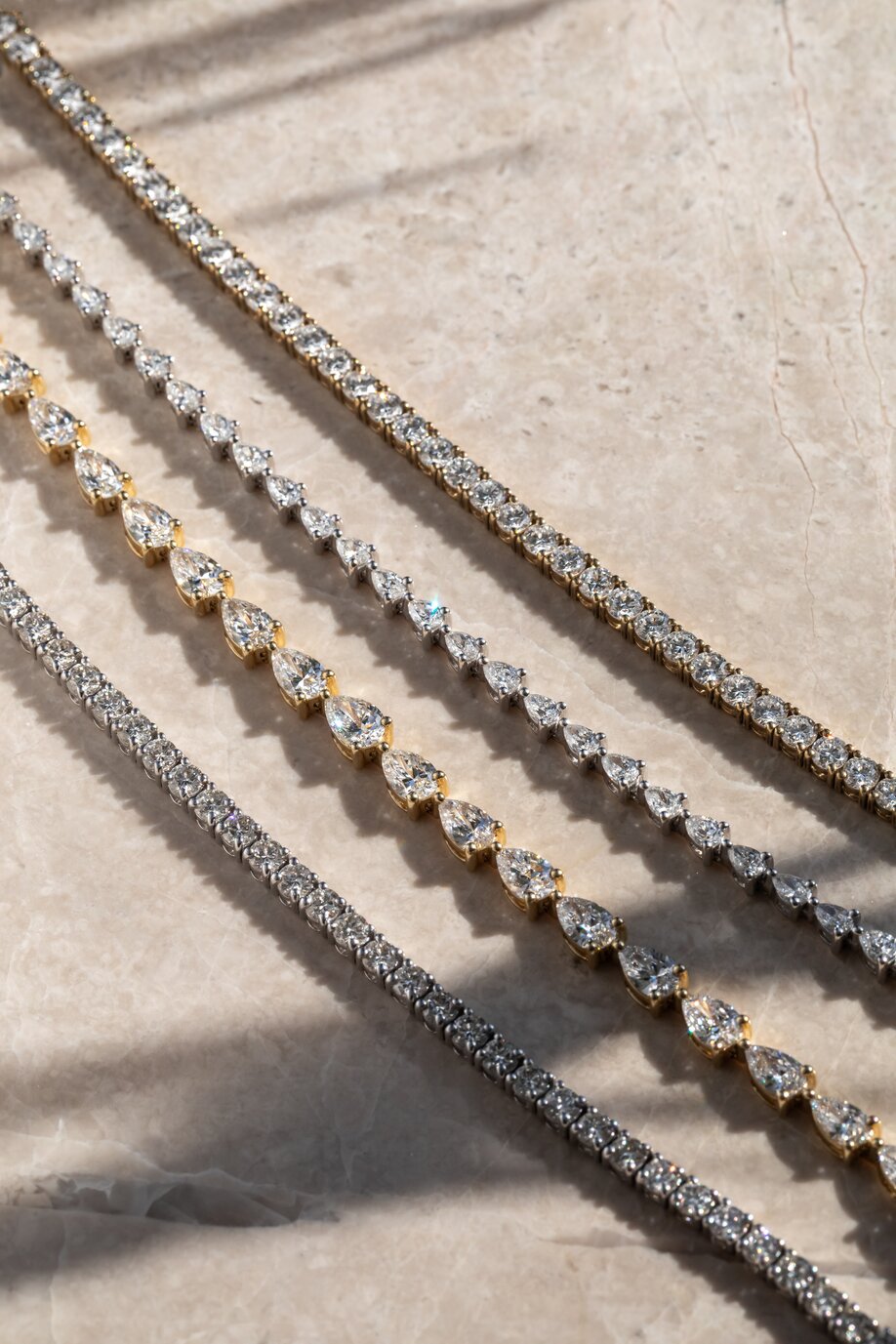 Mixed metal diamond tennis bracelets featuring round and pear-cut diamonds in elegant line settings