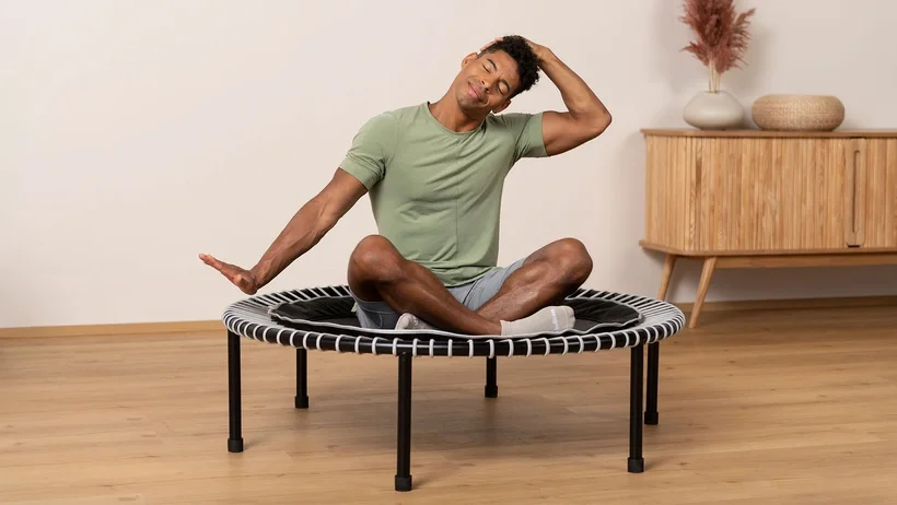 A man is stretching his neck on the bellicon rebounder.