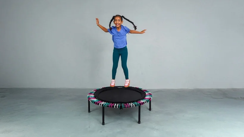 A girl happily jumping on a bellicon rebounder.