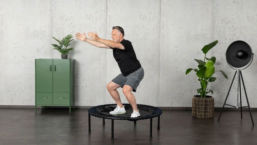 An older man is working out on the bellicon rebounder, holding a squat position.