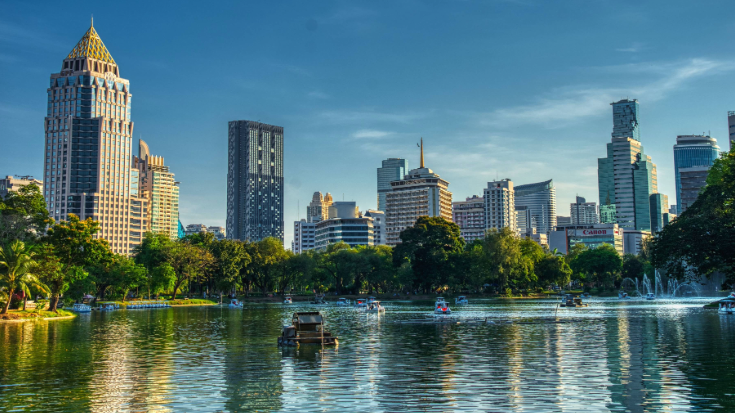 Een afbeelding van de skyline van Bangkok vanaf de overkant van een blauw meer in een stadspark. Er staan wolkenkrabbers langs de blauwe lucht – ter illustratie van een blogpost met de titel '33 leuke weetjes over Thailand'.