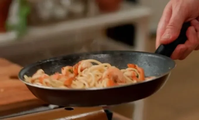 A person stirs pasta in a pan with a fork, showcasing the cooking ...