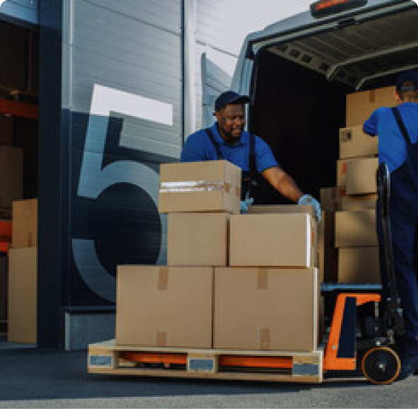 Man loading boxes off of a dolly and into a van. He is located behind a building with the number 5 painted on a black brick wall behind him. 