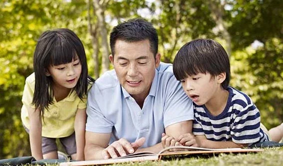 Dad lying on grass reading children book to his two young children