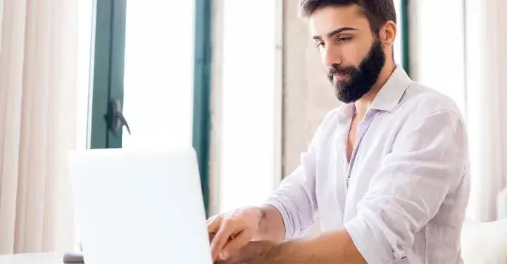 Bearded man typing at laptop with shirt pushed up to elbows