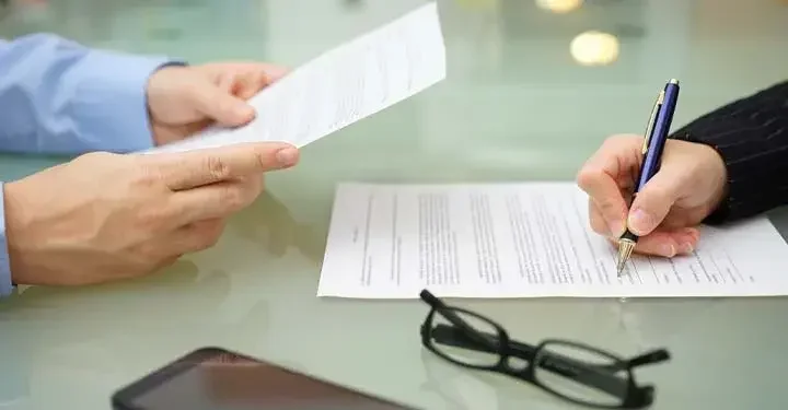 Hands holding a paper and another hand signing a document across the table