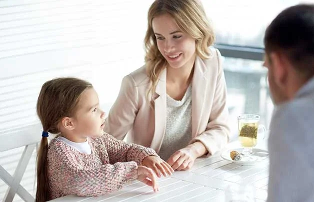 A mother sitting at a dining table with her daughter and new spouse. The new spouse is required to pay back child support from a previous marriage.