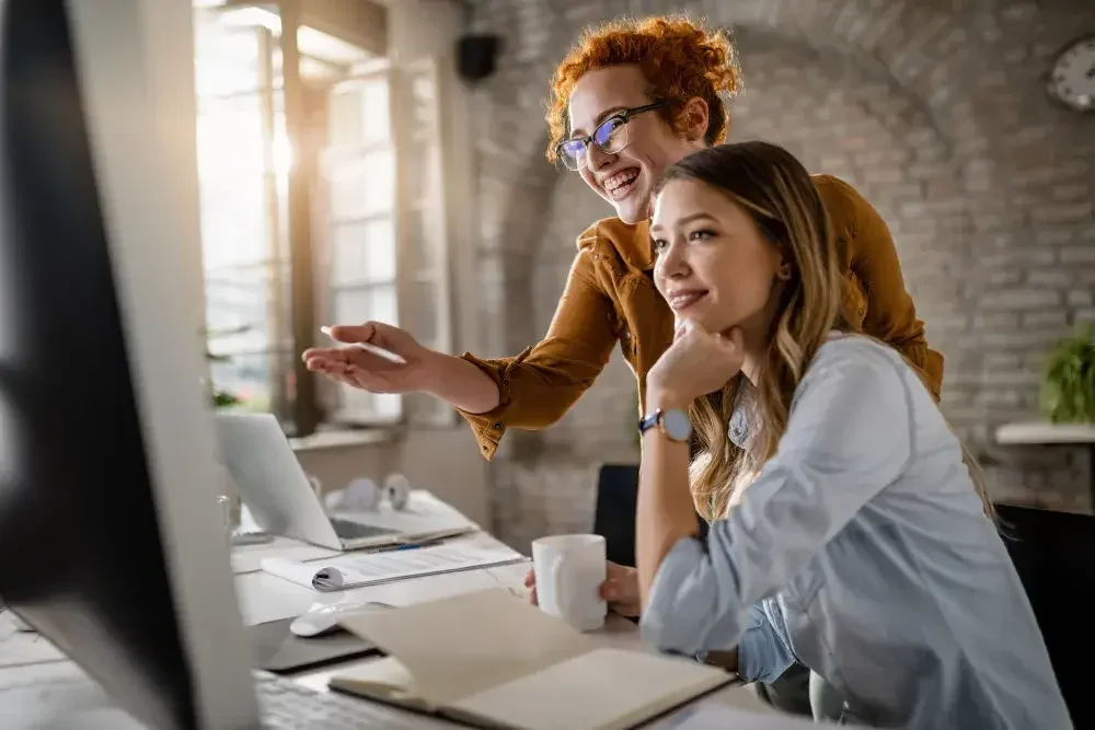 Two women look at a desktop computer screen as they check to see if the name they want to use for their new business is available.