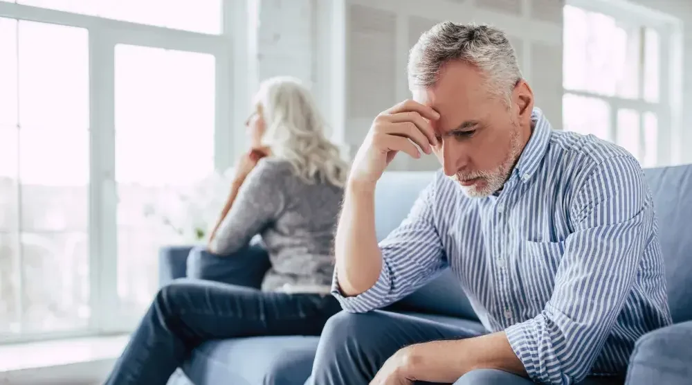 An older couple sits on opposite sides of a couch, seemingly upset because they are reaching the final stage in their divorce, which is the divorce decree.