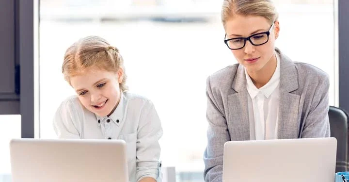 Daughter and mother sitting next to each other at a desk using respective laptops