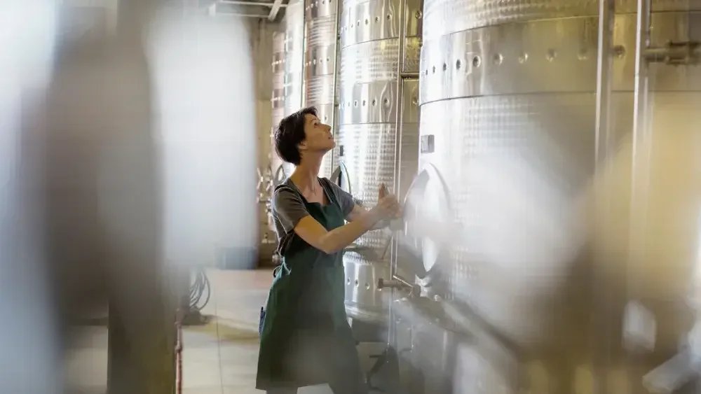 A woman adjusts levels on a distillery vat