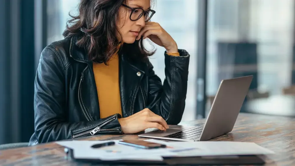 A woman wearing a leather jacket and eyeglasses looks at last will options online on her laptop computer.