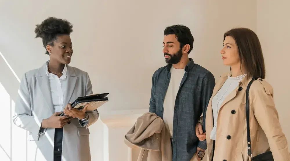 A contemplative couple stands in a sunny living room with a smiling woman holding a clipboard. There are multiple ways to avoid capital gains taxes on your inherited property.