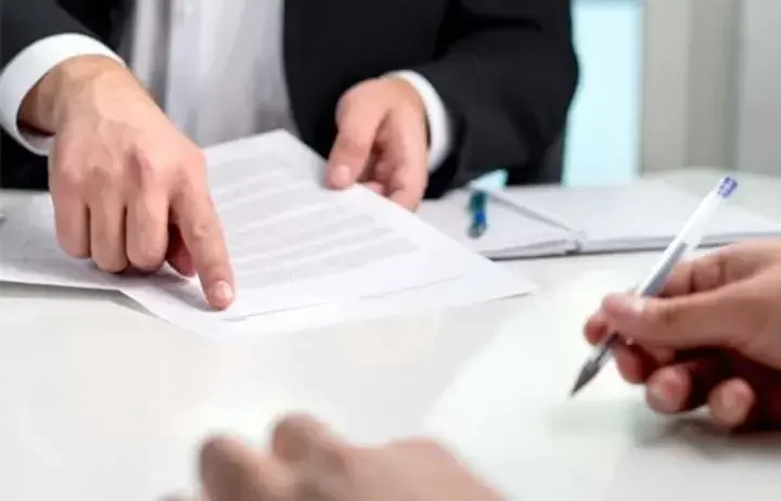 Man points at word on document across from table of man with blue ballpoint pen