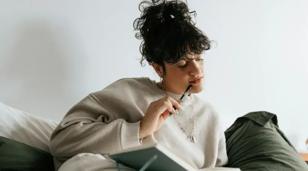 Woman sits on her bed with a pen to her lips as she looks at a list of names in her journal. How long it takes to change your name will depend on quite a few factors.