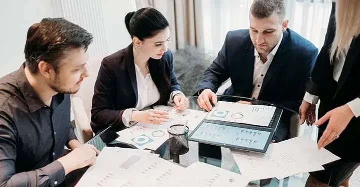 Businesspeople sitting around table and looking at graphs on papers and computers