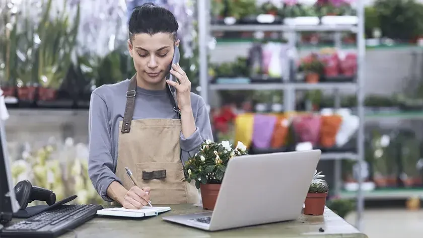 woman in flower shop wearing brown apron taking an order on the phone